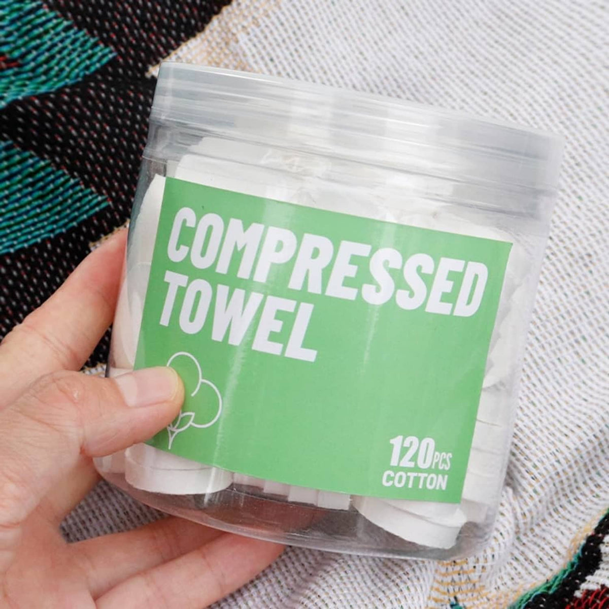 Hand holding compressed towel pouch, green label, white 120 pcs cotton towels