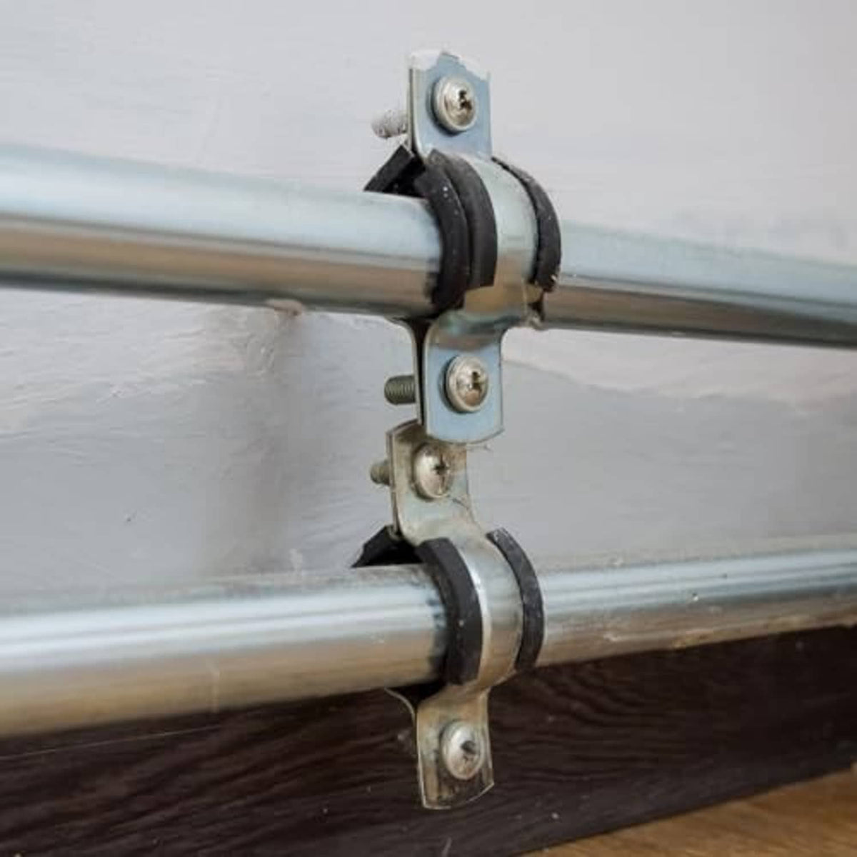 Black rubber split-ring clamp securing metal pipes with zinc bolts and brackets