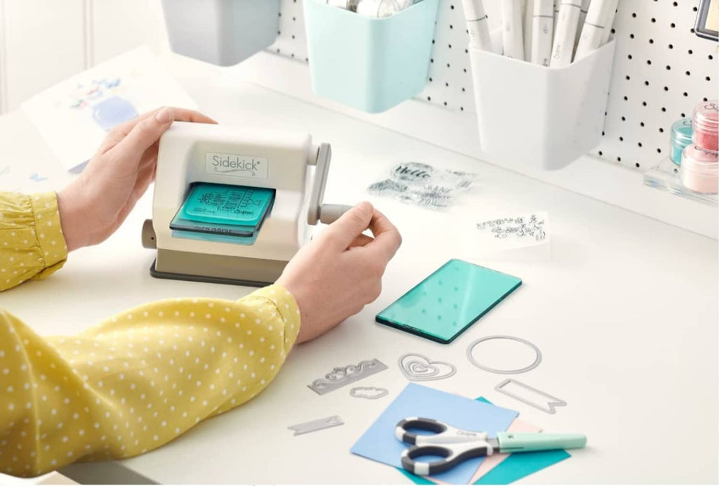 White die-cutting machine with teal plate, cutting dies, and prepared cards