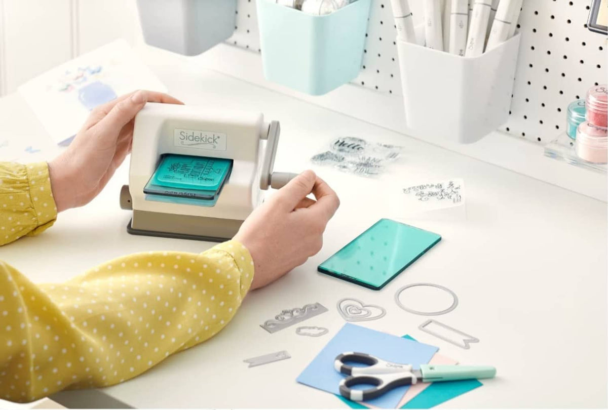 White die-cutting machine with teal plate, cutting dies, and prepared cards