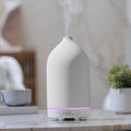 White ceramic essential oil diffuser with pink LED light strip on a tabletop base.