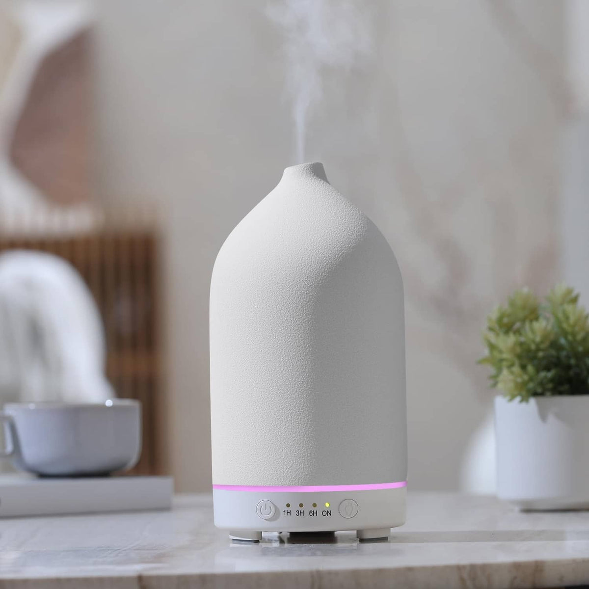 White ceramic essential oil diffuser with pink LED light strip on a tabletop base.