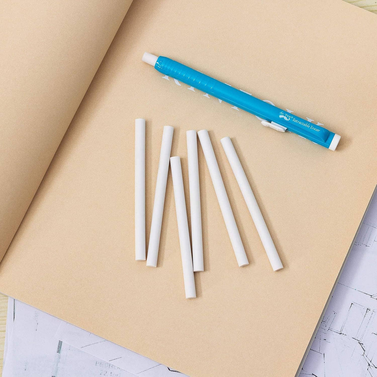White eraser refill sticks with a blue retractable mechanical pen on brown paper