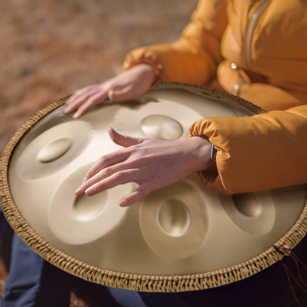 Golden handpan drum with hands resting on the tone surface, raised note dimples