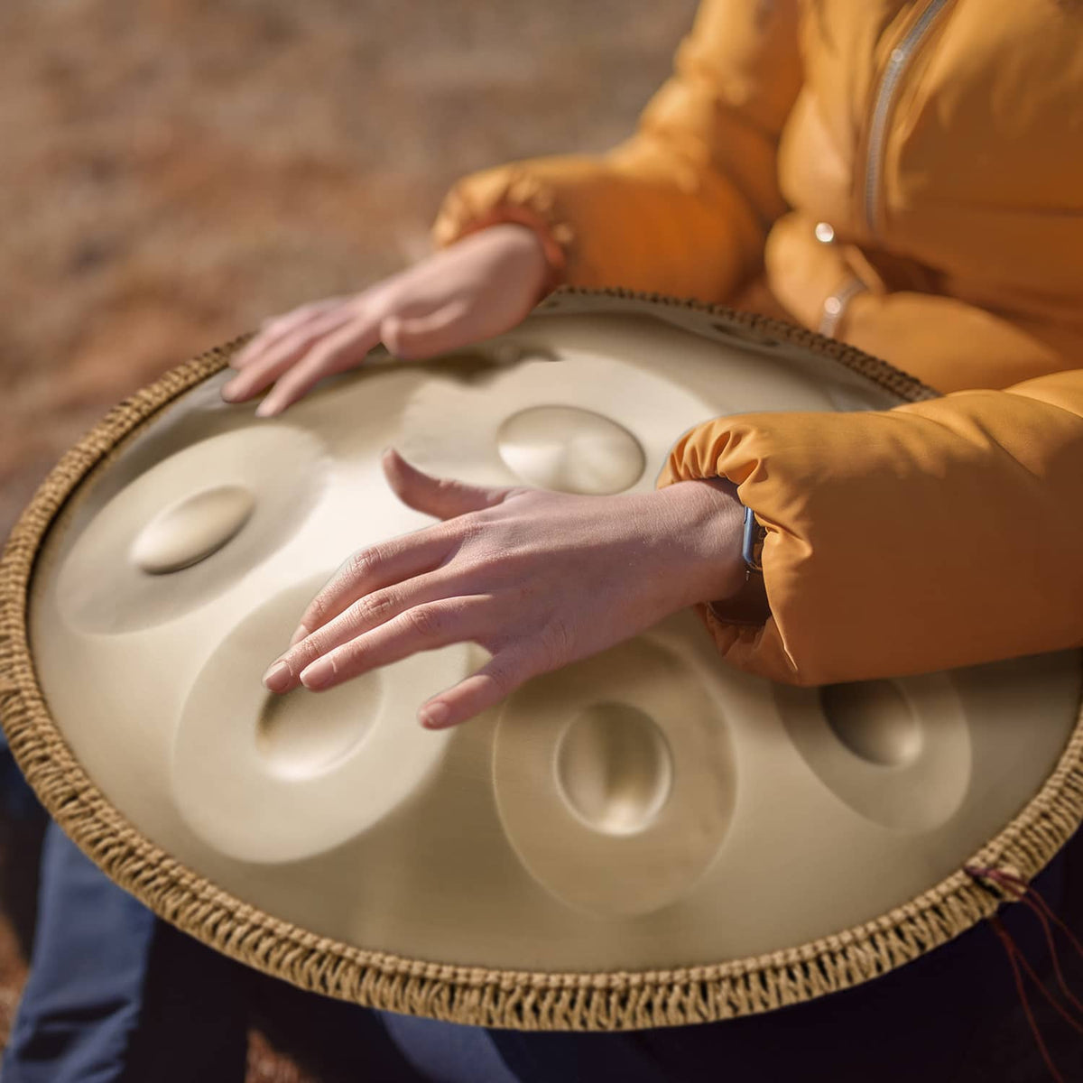 Golden handpan drum with hands resting on the tone surface, raised note dimples