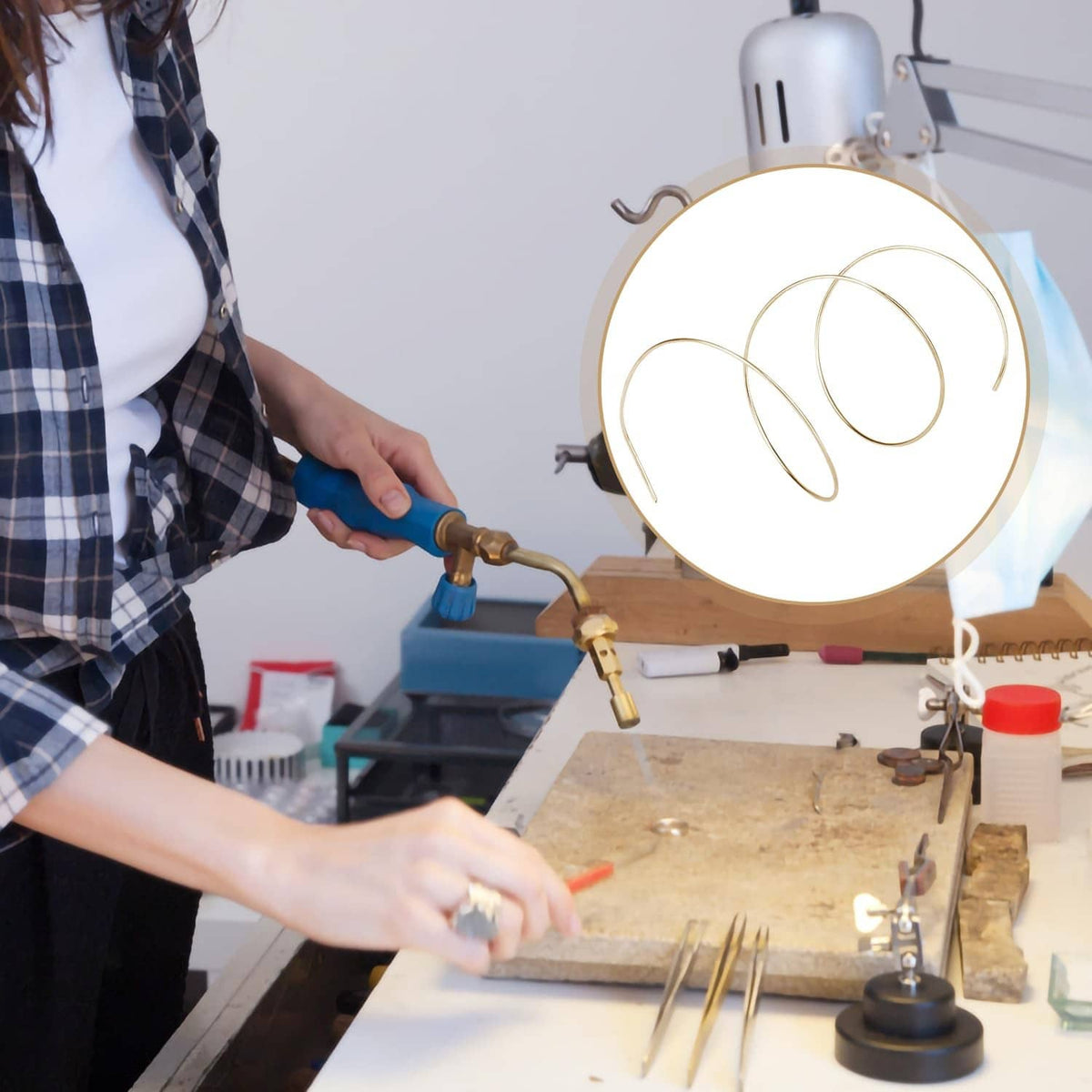 Gold-plated solder wire coil on workspace, being handled for jewelry soldering