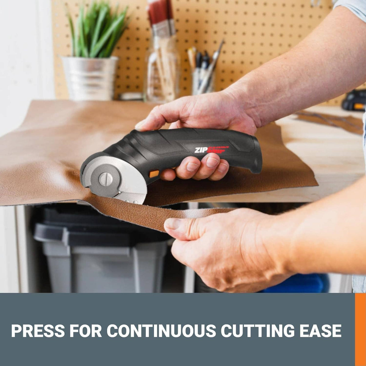 Electric scissors held by hand cutting brown cardboard on a work surface