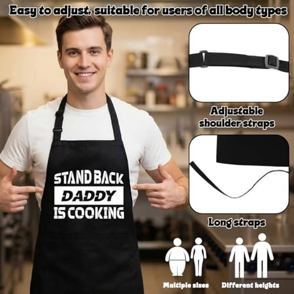 Black adjustable apron showing shoulder straps and long ties; “STAND BACK DADDY IS COOKING”