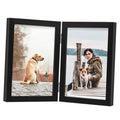 Black double hinged wooden photo frame with clear glass, open, displaying two photos