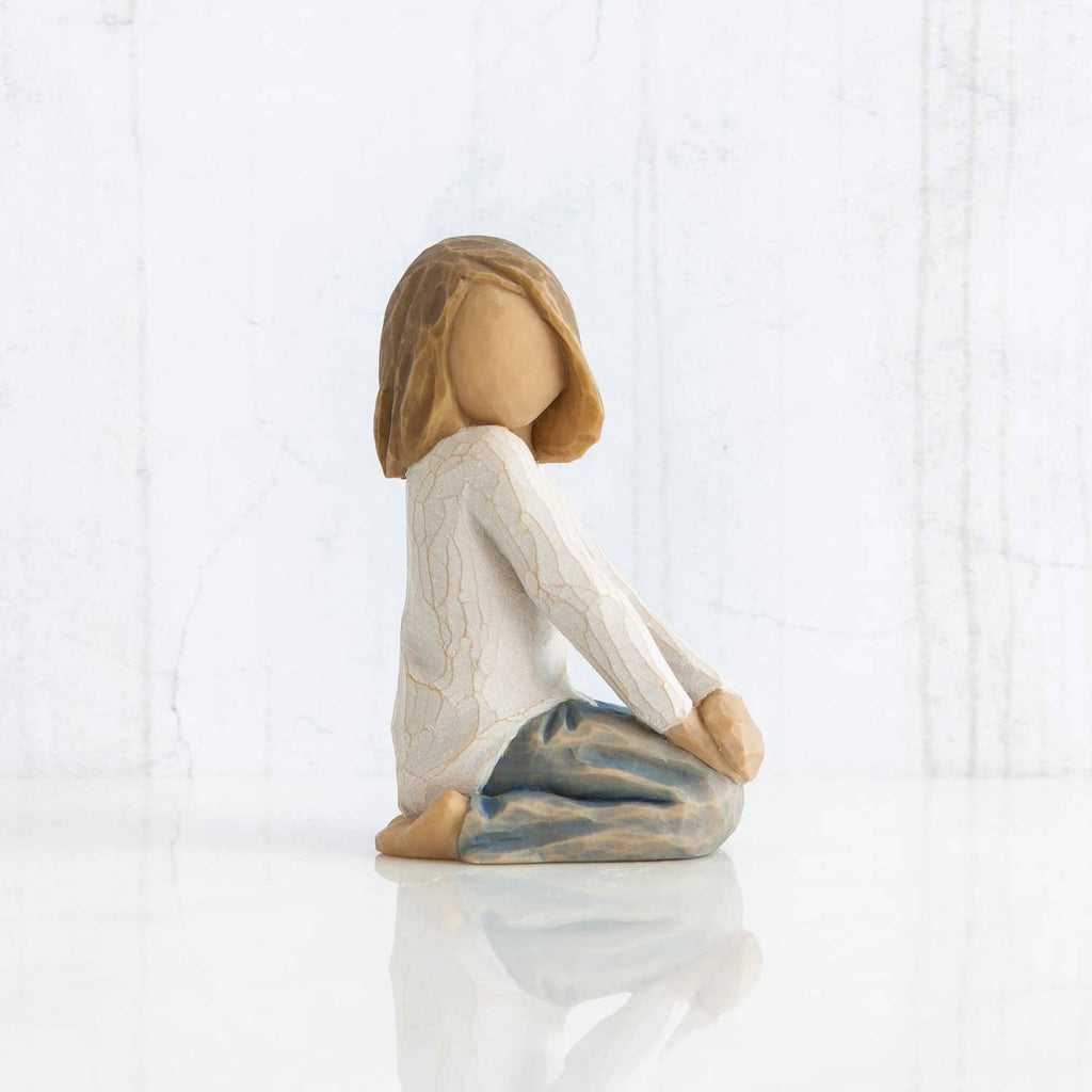 Kneeling child figurine with brown hair and white robe, blue-gray blanket, side view.