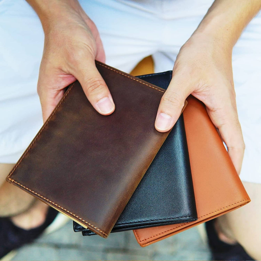 Brown leather travel wallet, bi-fold open and held by hands, stitched edges visible