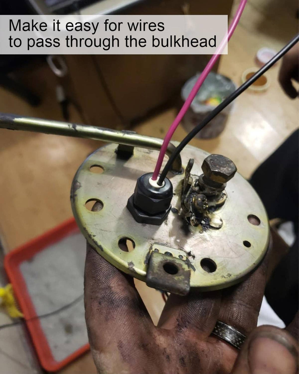 Black bulkhead fitting installed on metal panel with wires passing through