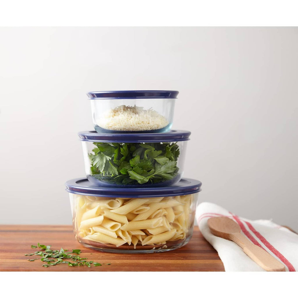 Three clear glass food storage containers with navy-blue lids, filled with pasta and greens