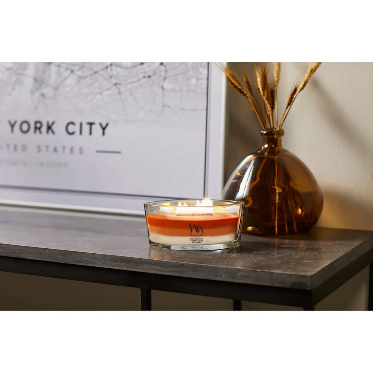 Lit orange wax jar candle on a dark shelf surface