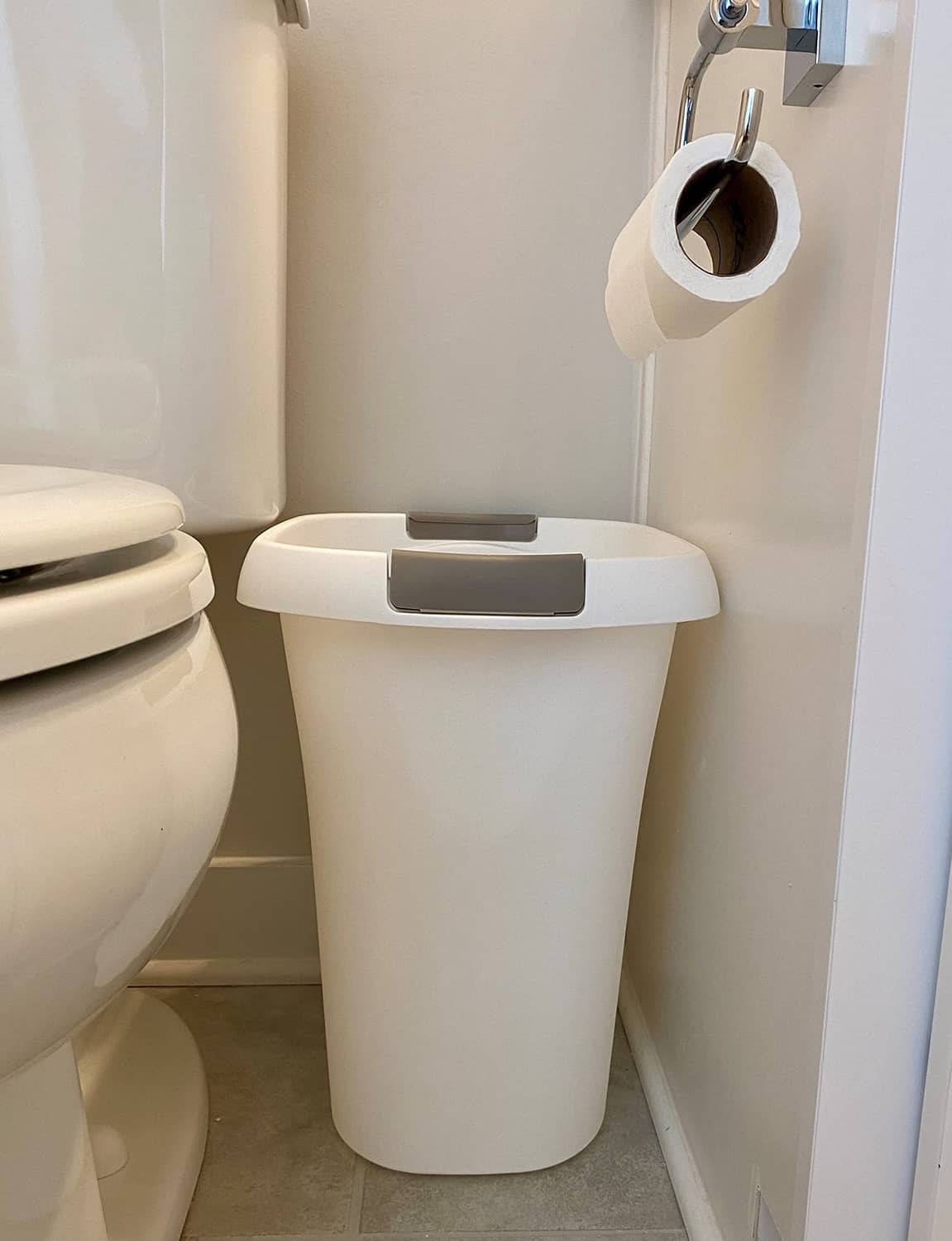 White plastic open-top trash can with gray lid near bathroom fixture