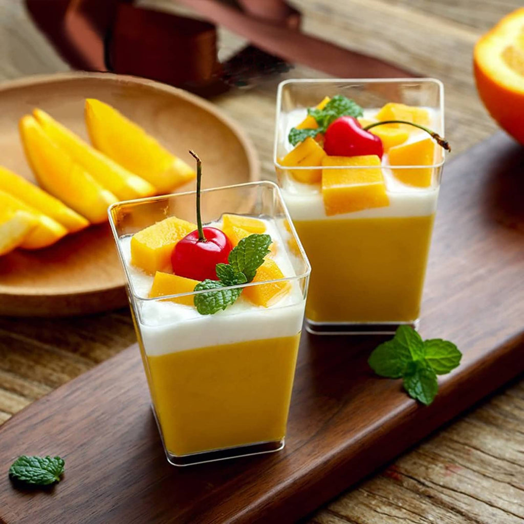 Tall clear square cups with spoons, filled with orange and white layered dessert