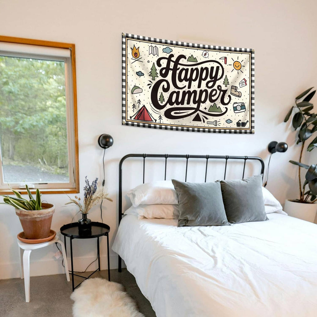 “Happy Camper” banner flag with illustrated camping icons and brass grommets above bed