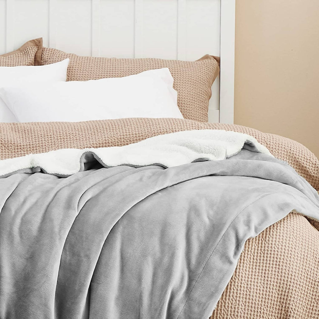 Light grey sherpa fleece throw blanket on bed with textured edge detail