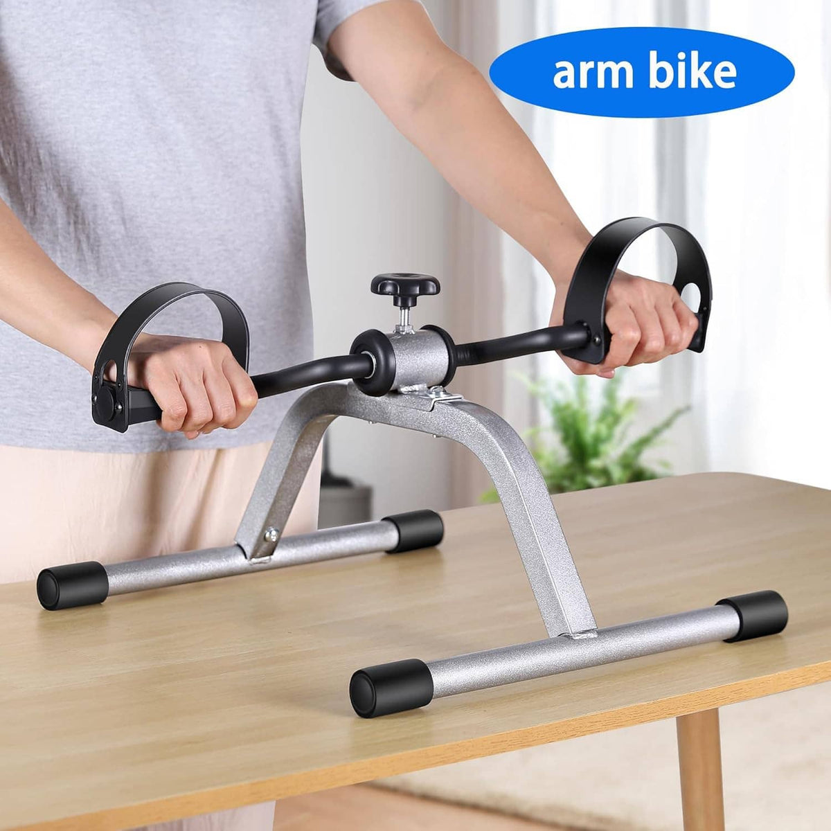 Mini exercise pedal bike in use with hands on black arm handles and seat stem