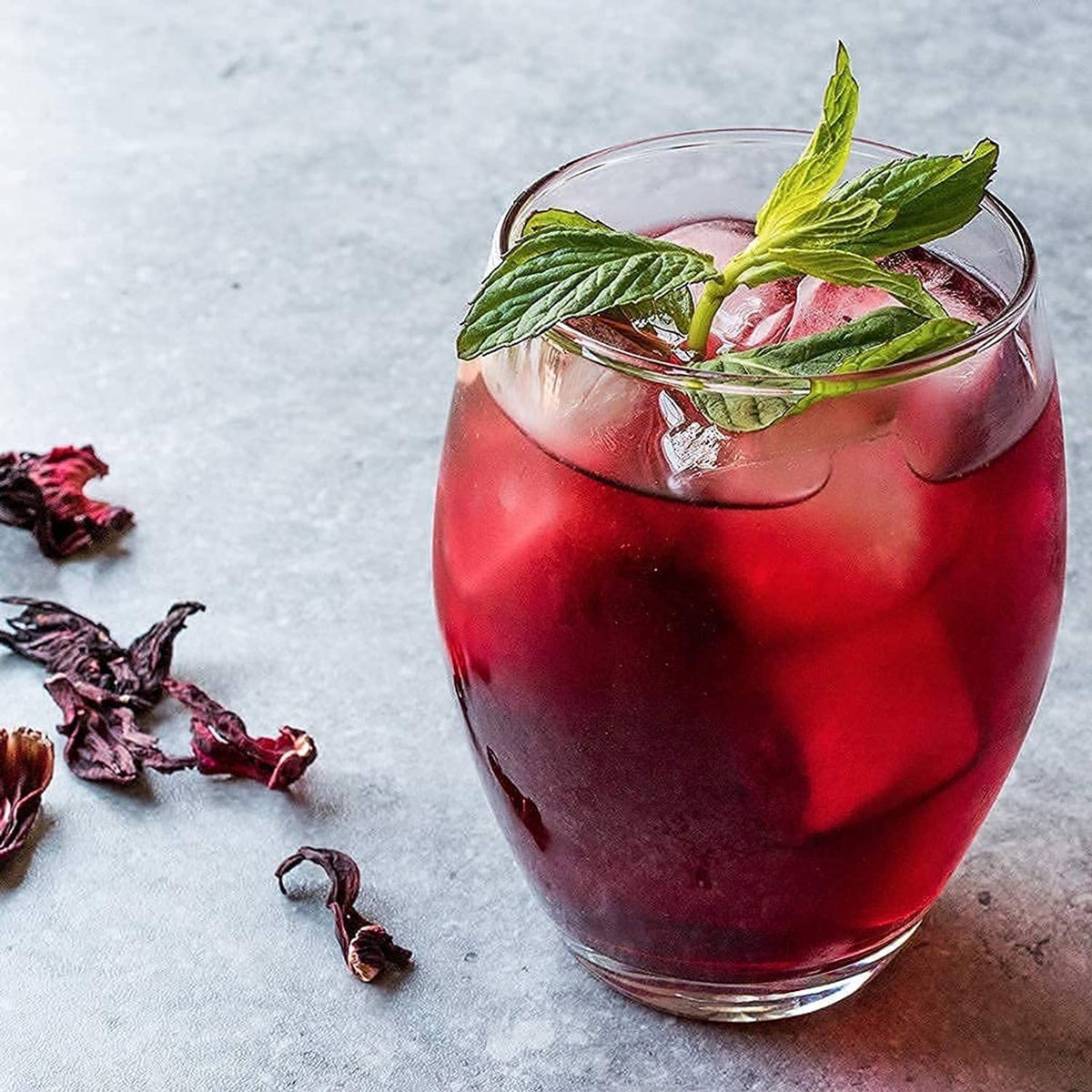 Iced hibiscus tea in a glass with mint and dried petals