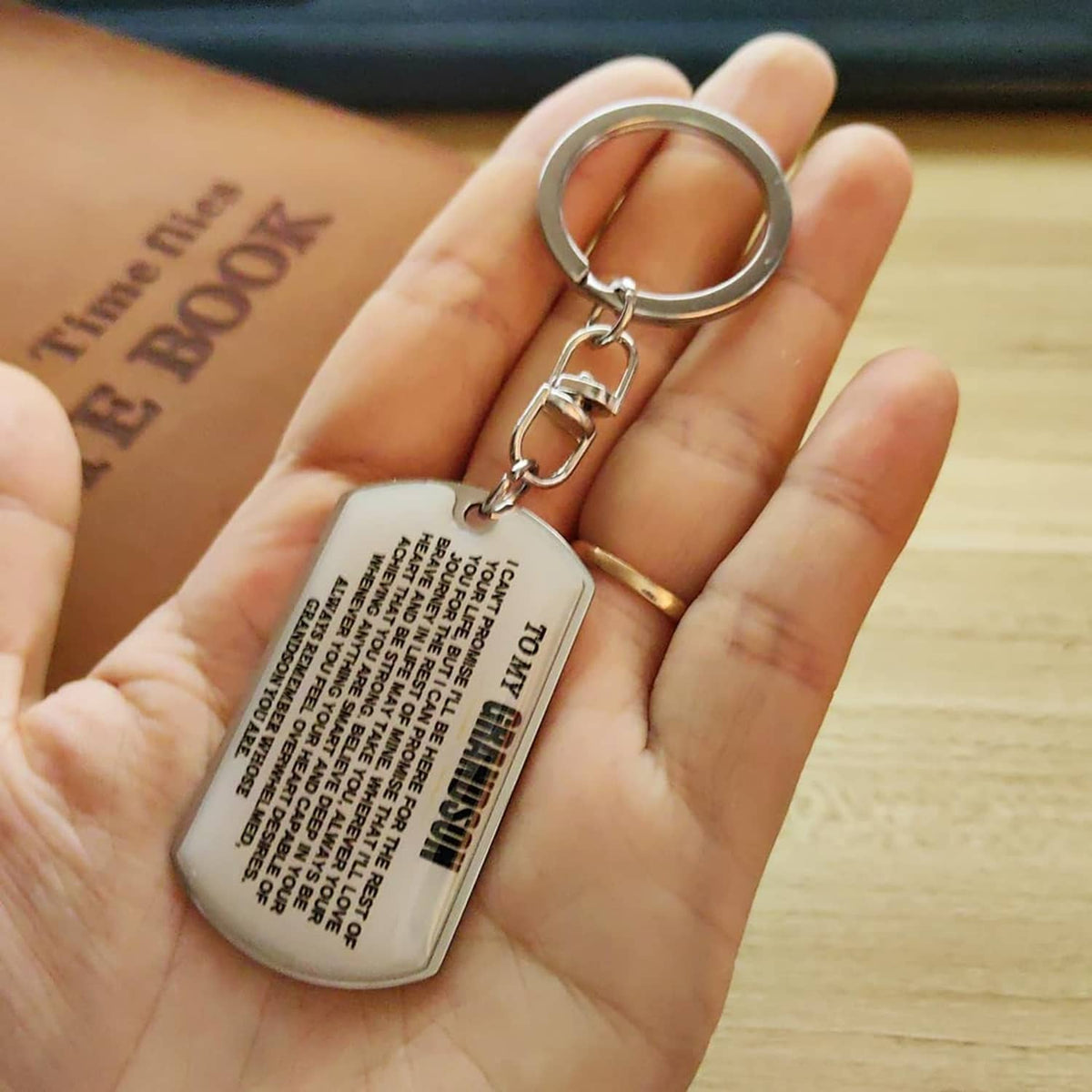 Silver dog-tag keychain held in hand, engraved inspirational message