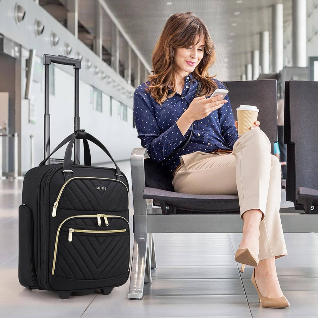Black softside carry-on suitcase with gold-trim front zipper, beside seated woman