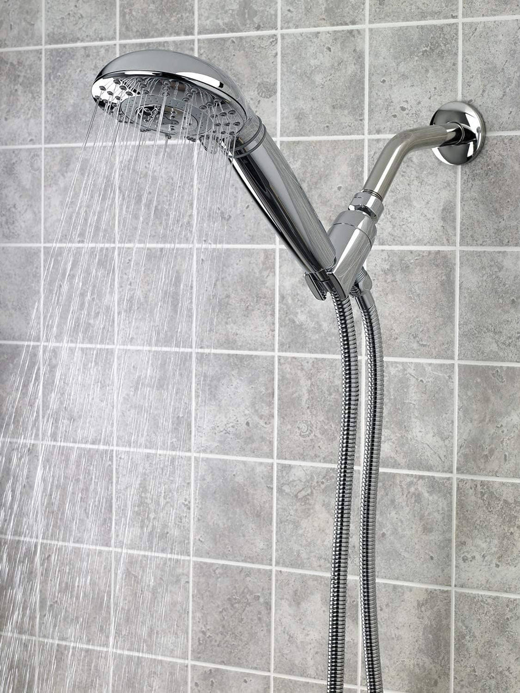 Chrome shower head and flexible hose on tiled wall with water spray