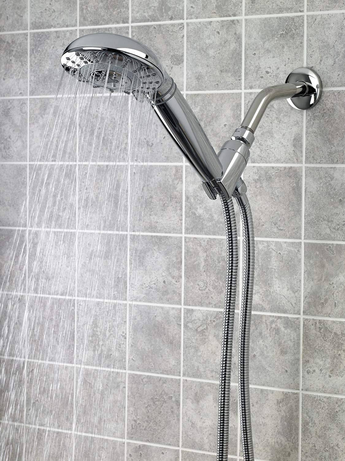 Chrome shower head and flexible hose on tiled wall with water spray