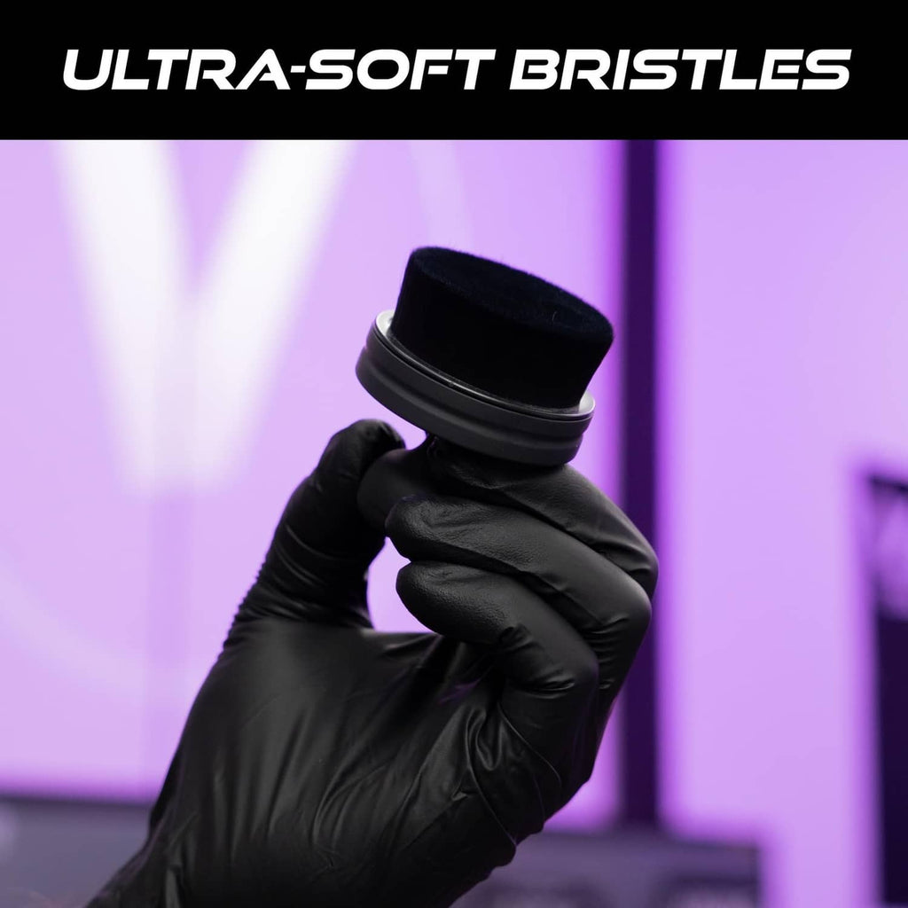 Black tire shine applicator brush with fine bristles held by a gloved hand