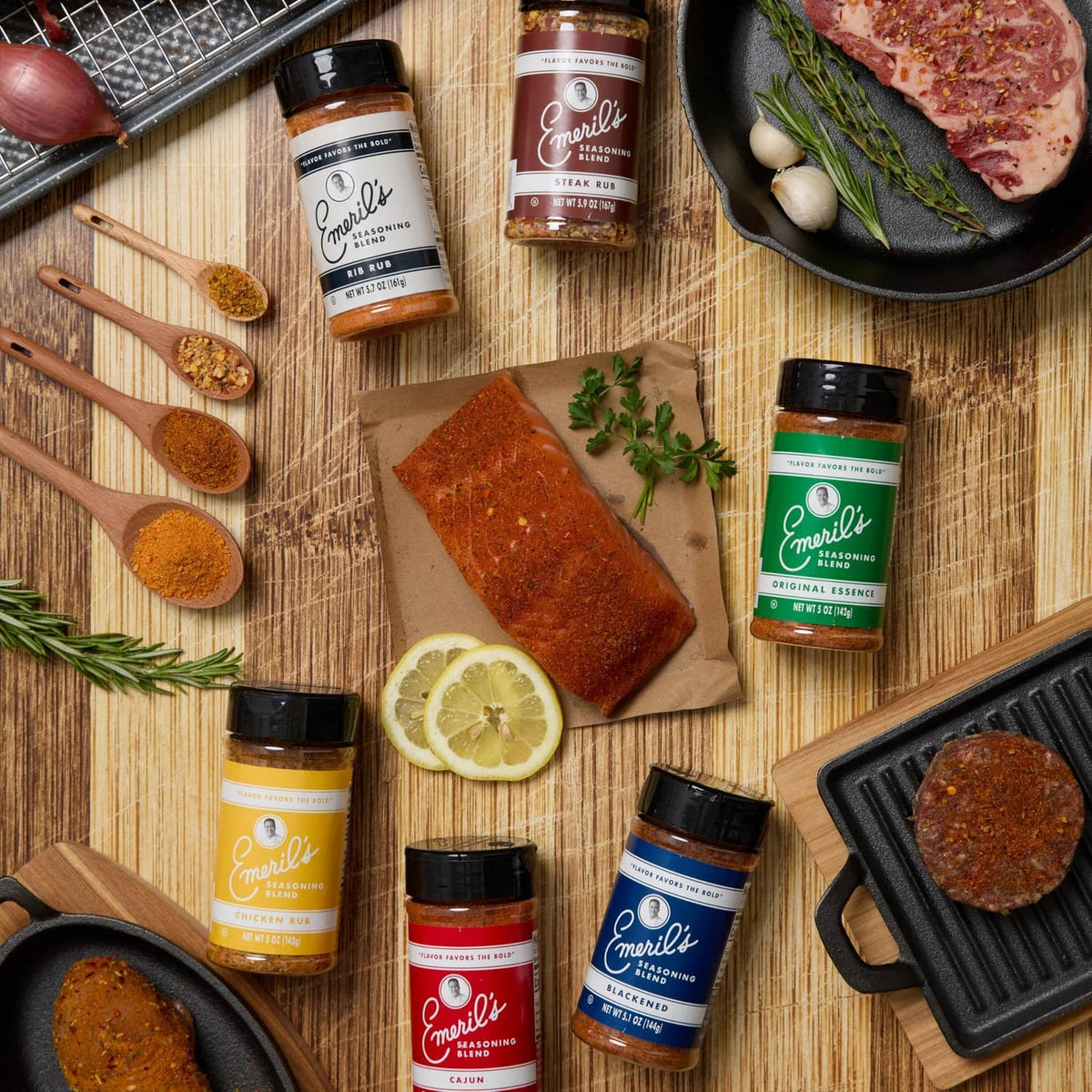 Pack of Emeril's seasoning jars with spices and grilled foods on a countertop