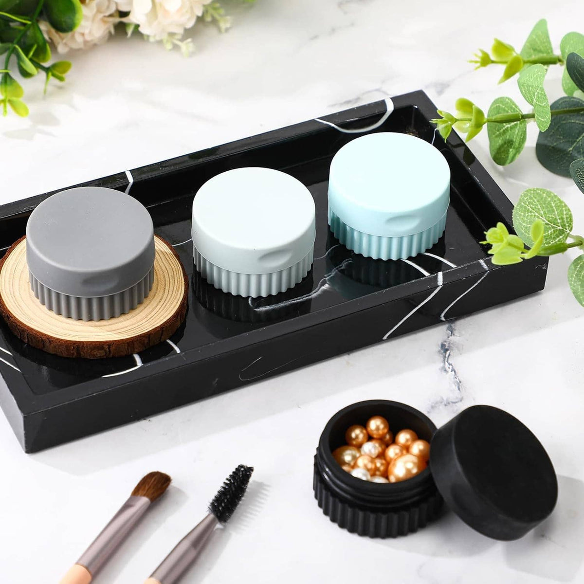 Four small silicone travel jars in black and light colors in a hinged carrying tray