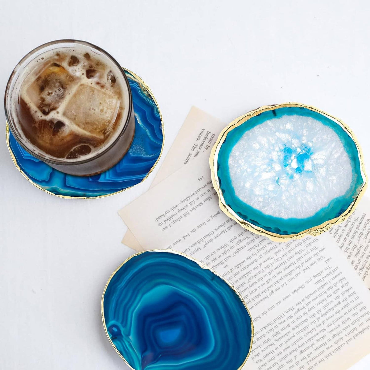 Blue agate-style coasters holding glasses on white papers with gold-tone edges.
