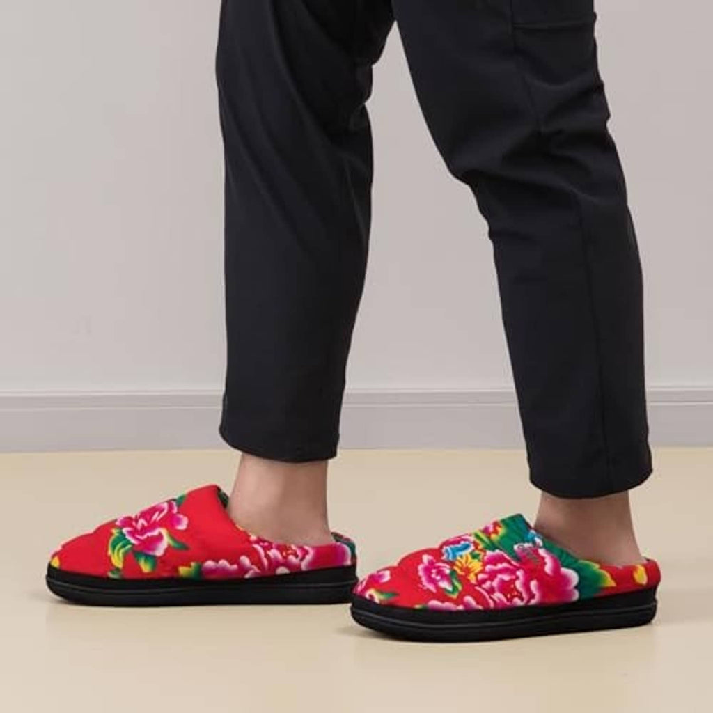 Men's floral slip-on slippers in red with green lining and black soles, worn on feet.