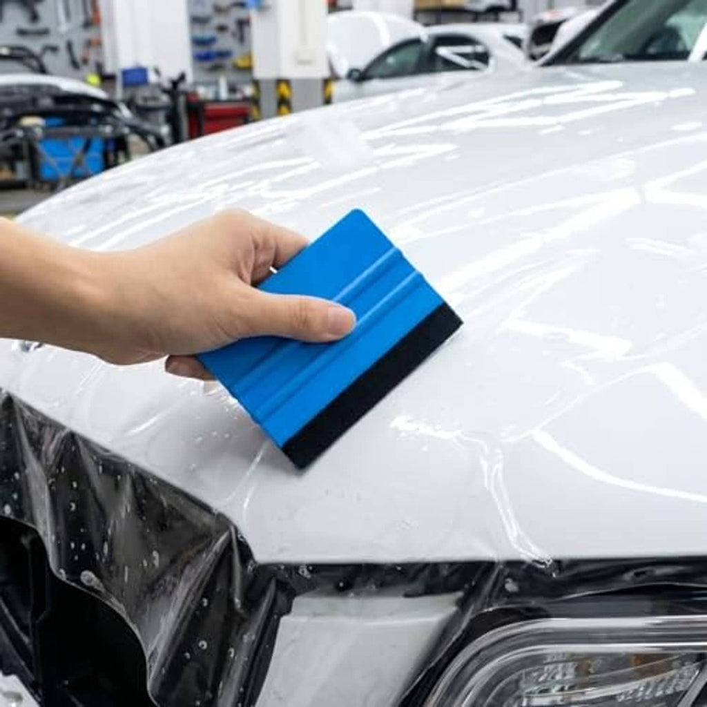Blue felt-edged squeegee smoothing window privacy film on a car hood