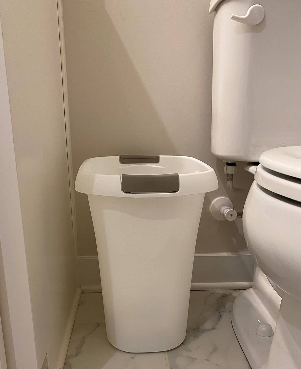 White plastic open-top trash can with gray lid next to toilet