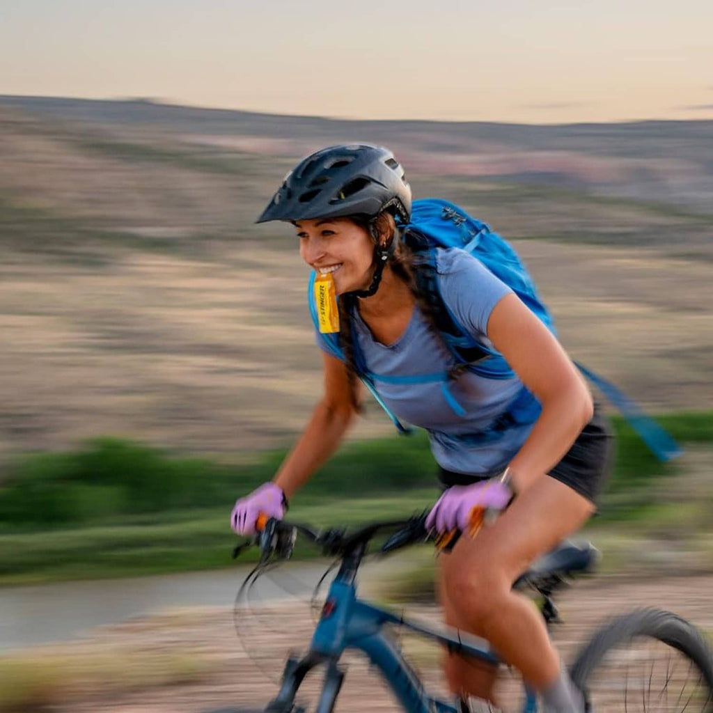 Cyclist drinking from Honey Stinger energy gel packet while riding