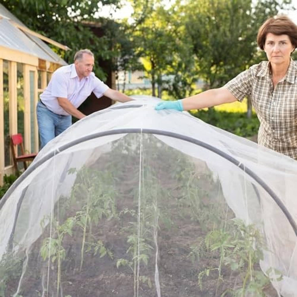 White mesh greenhouse cover being installed over a garden