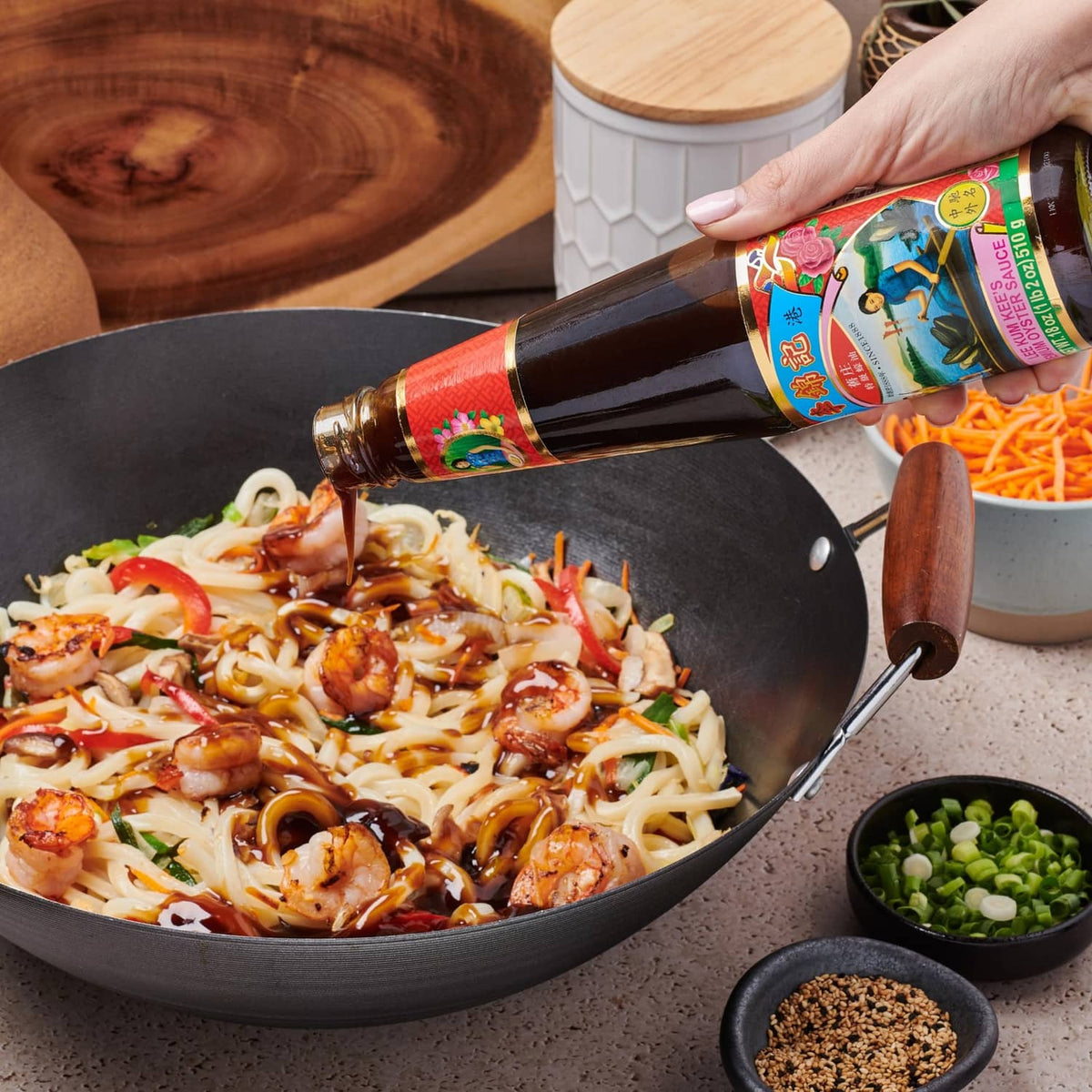 Oyster sauce bottle drizzling into a pan of stir-fried noodles and seafood