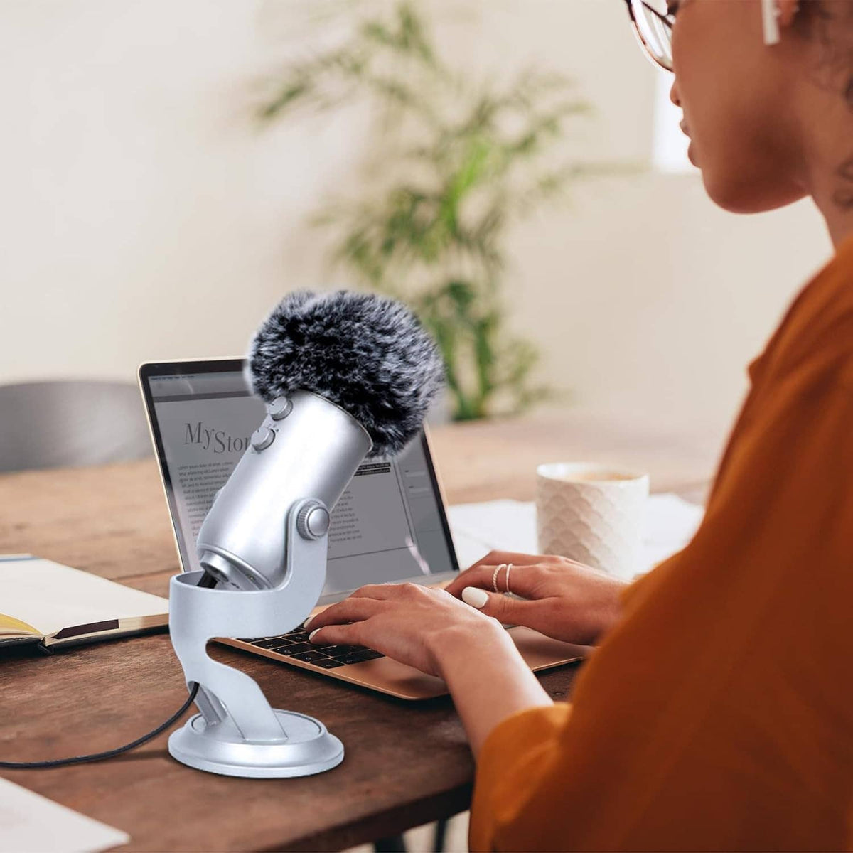 Gray furry windscreen pop filter on microphone at a desk, angled for voice recording