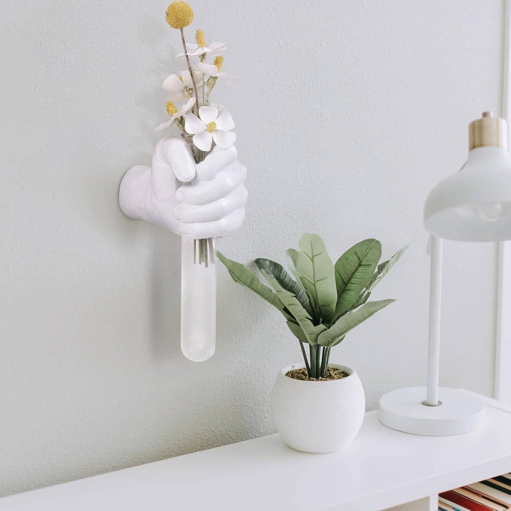 White hand vase wall hanging holding white blossoms with green leaves