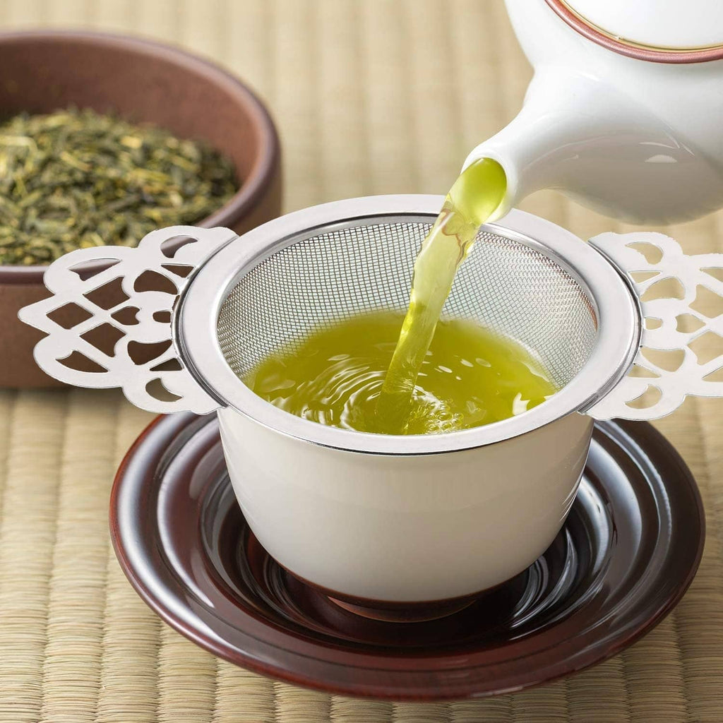 Tea infuser with green tea dripping into white cup on top of drip bowl