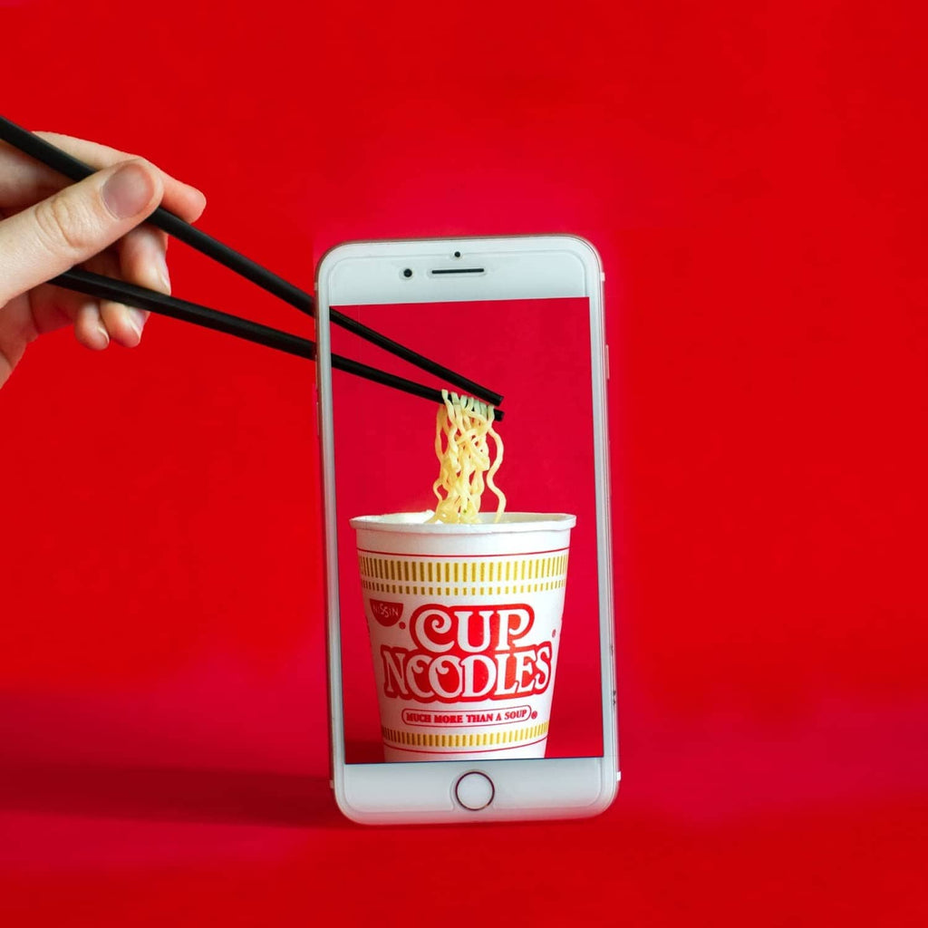 Nissin Cup Noodles chicken-flavor cup on smartphone screen with chopsticks