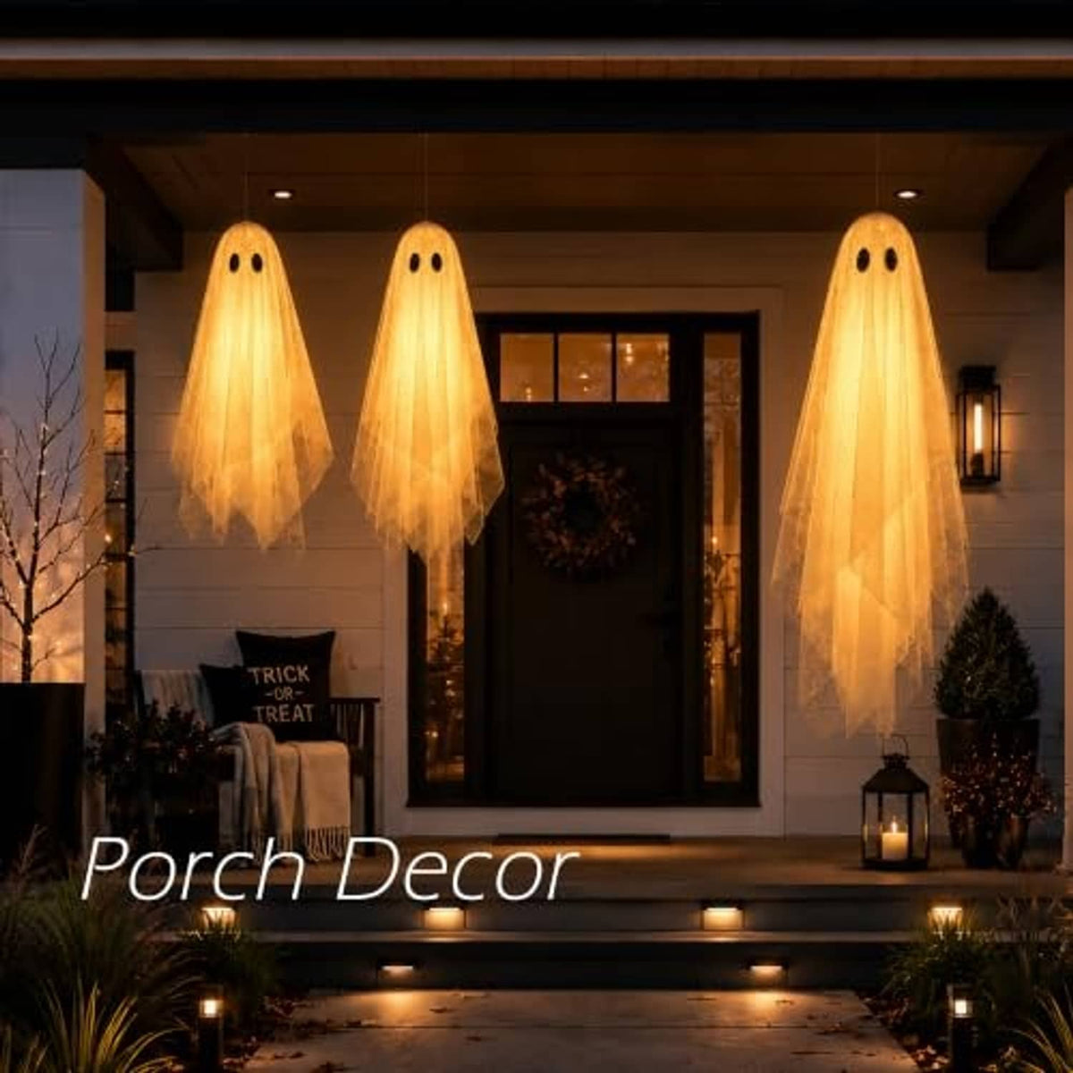 Three warm-lit hanging ghost decorations on a porch with sheer tails and black eyes