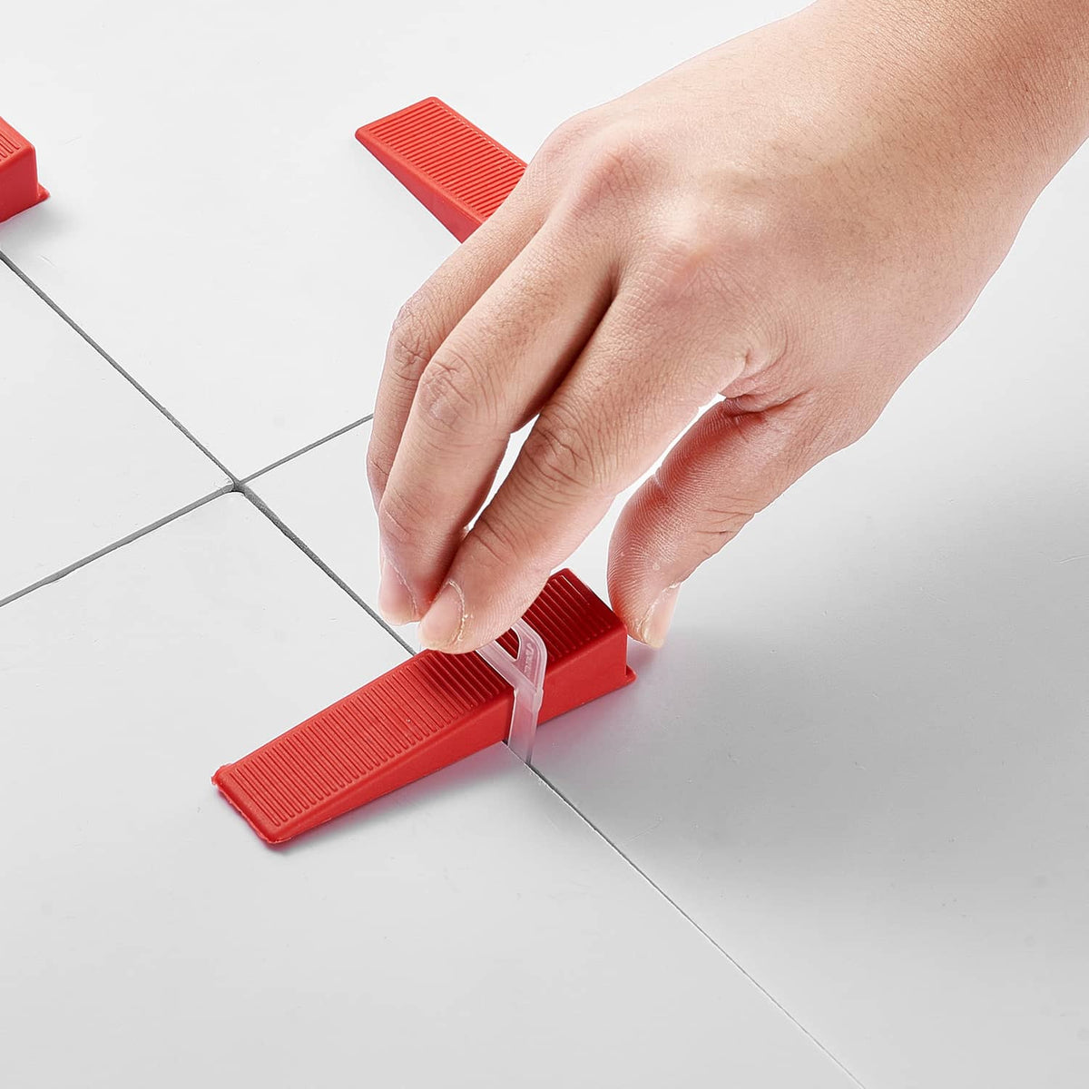 Hand pressing a red tile leveling spacer clip between two floor tiles