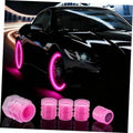 Set of pink glow-in-the-dark tire valve caps next to a car wheel and fender