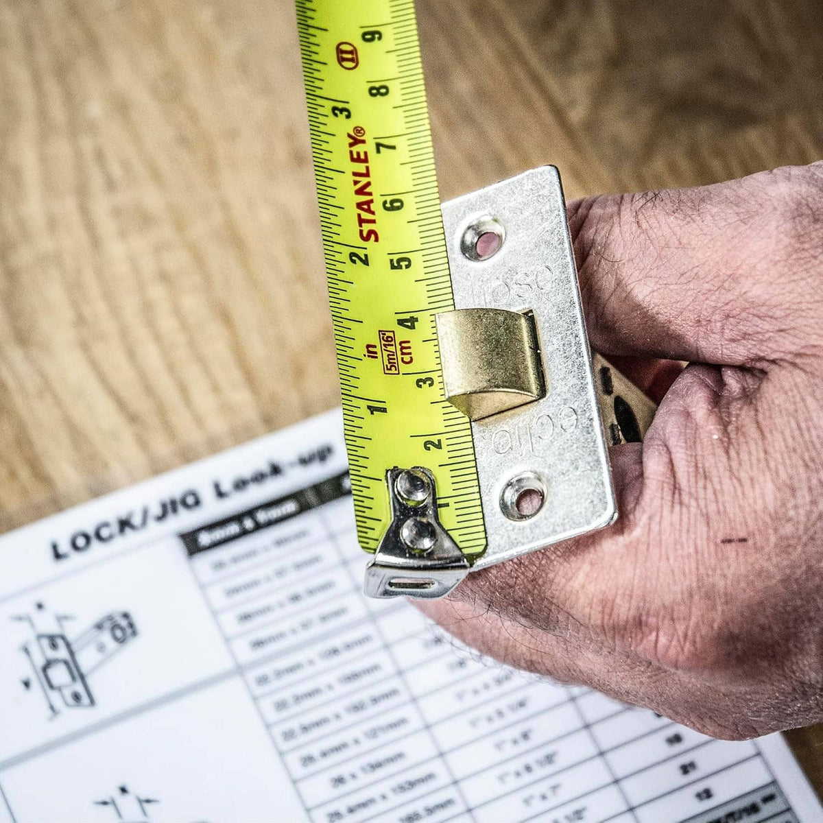 Metal lock jig template plate held by a hand with yellow measuring tape