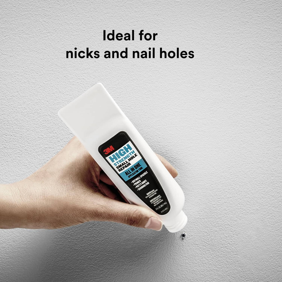 White applicator tube in hand dispensing repair into a small wall hole