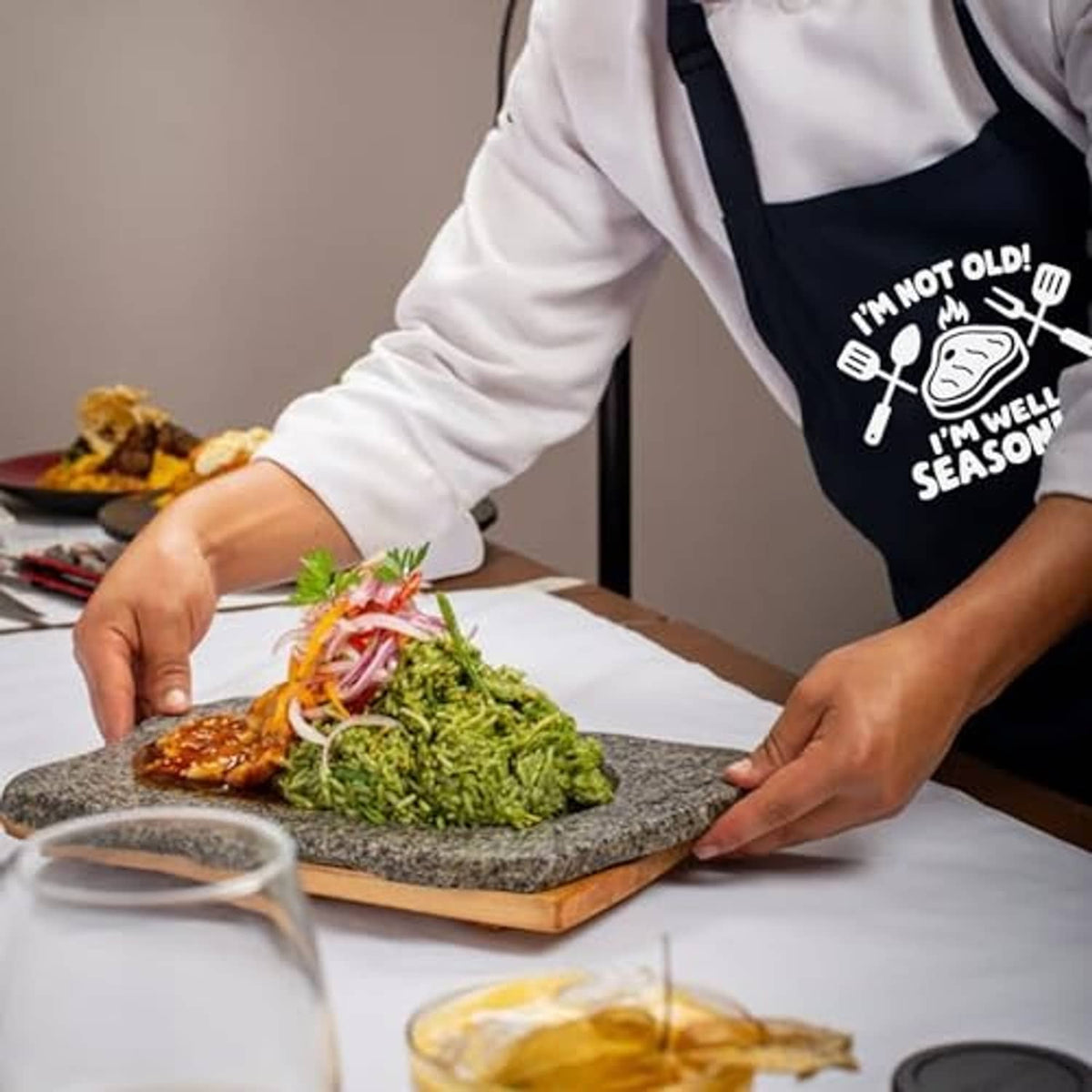 Black apron with cooking graphic as hands prep and season food on a cutting surface