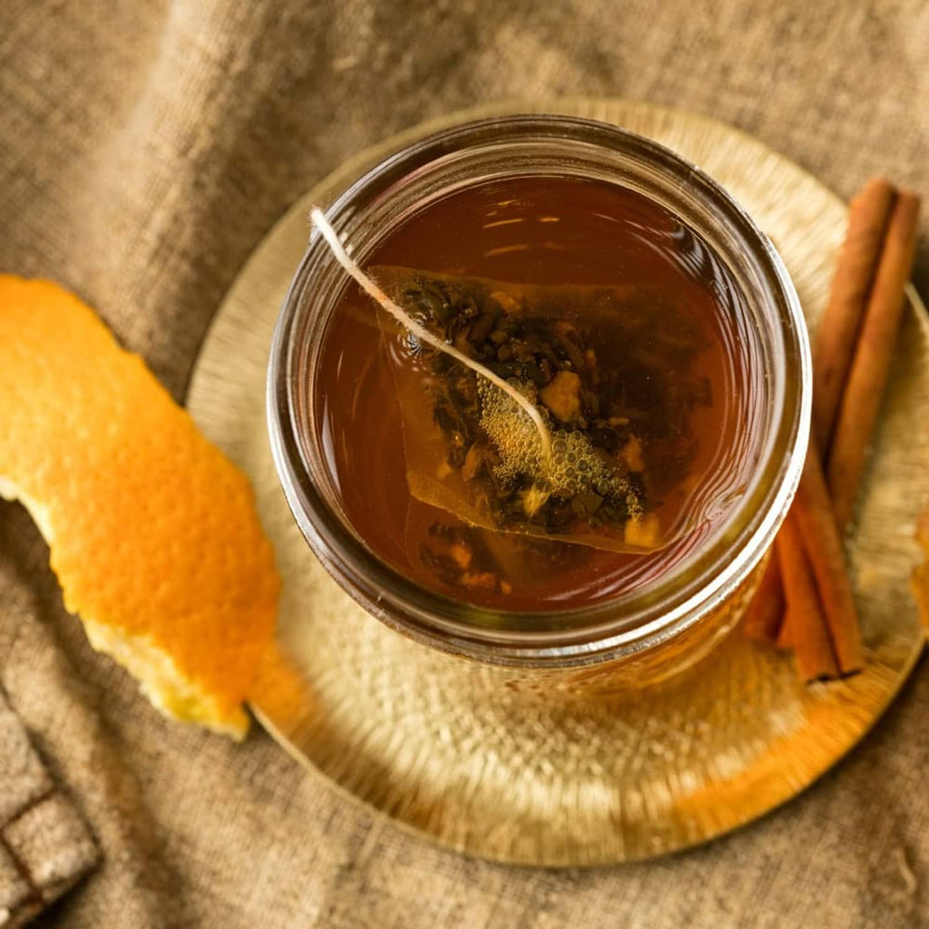 Jar of brewed tea with tea leaves and cinnamon sticks on a wooden plate