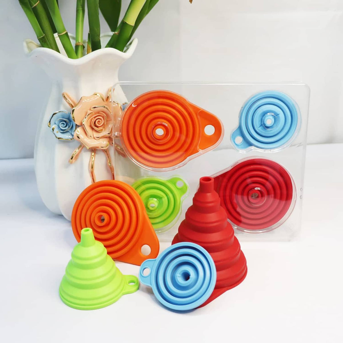 Foldable silicone kitchen funnel set in red, orange, blue, and green inside a clear storage box